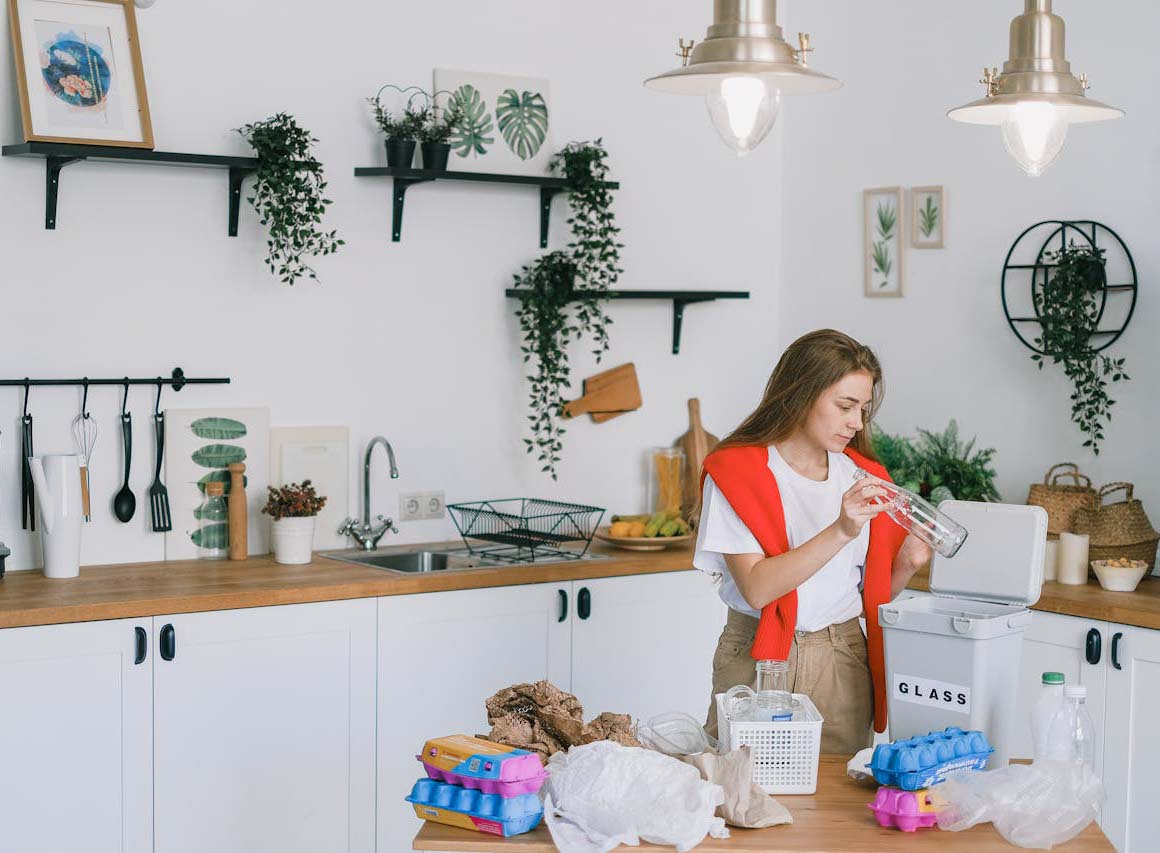Woman sorting waste into kitchen trash can, showing recycling habits