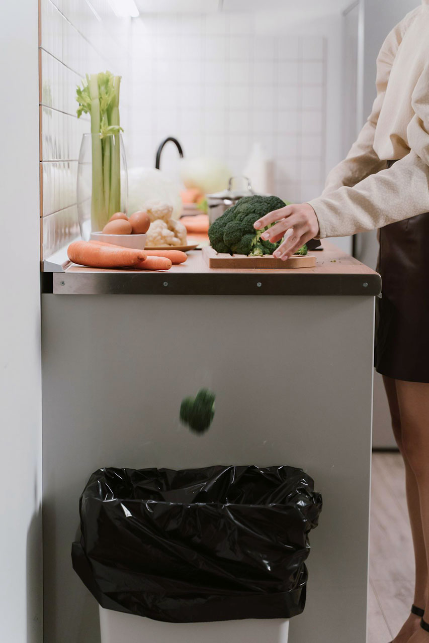 Slim freestanding trash can tucked near the counter edge in a compact kitchen