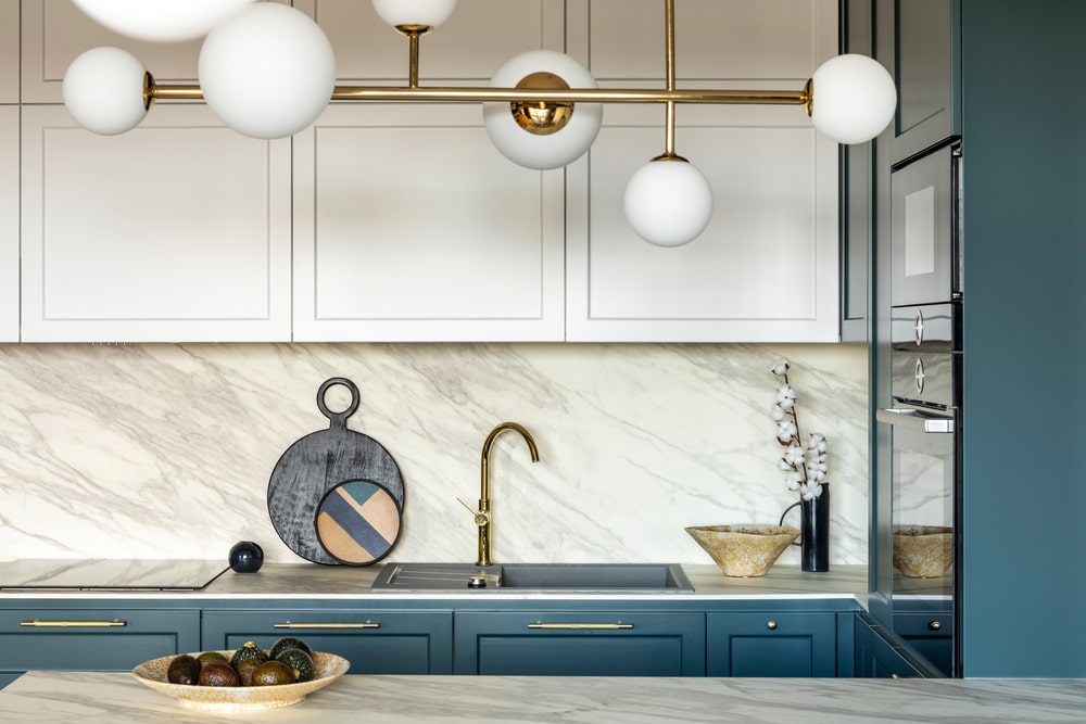 dark teal and white kitchen cabinets with gold hardware and modern lighting fixture