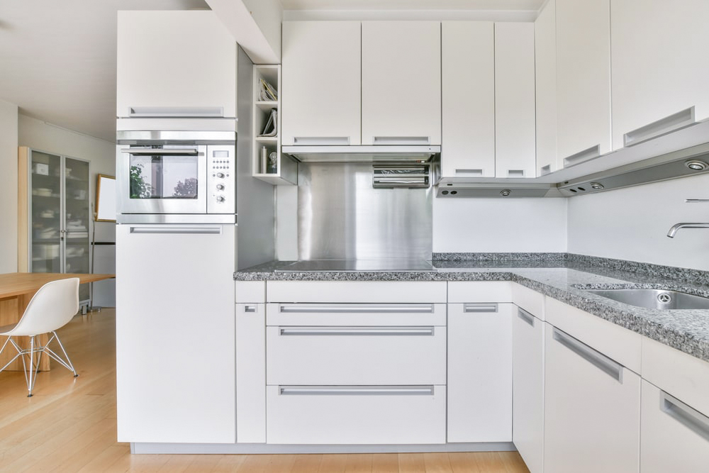 white cabinets, stained steel backsplash and granite countertop in condo small kitchen